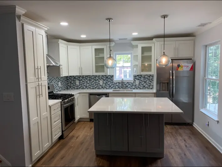 Finished kitchen remodel with island, white cabinets, backsplash, and pendant lighting